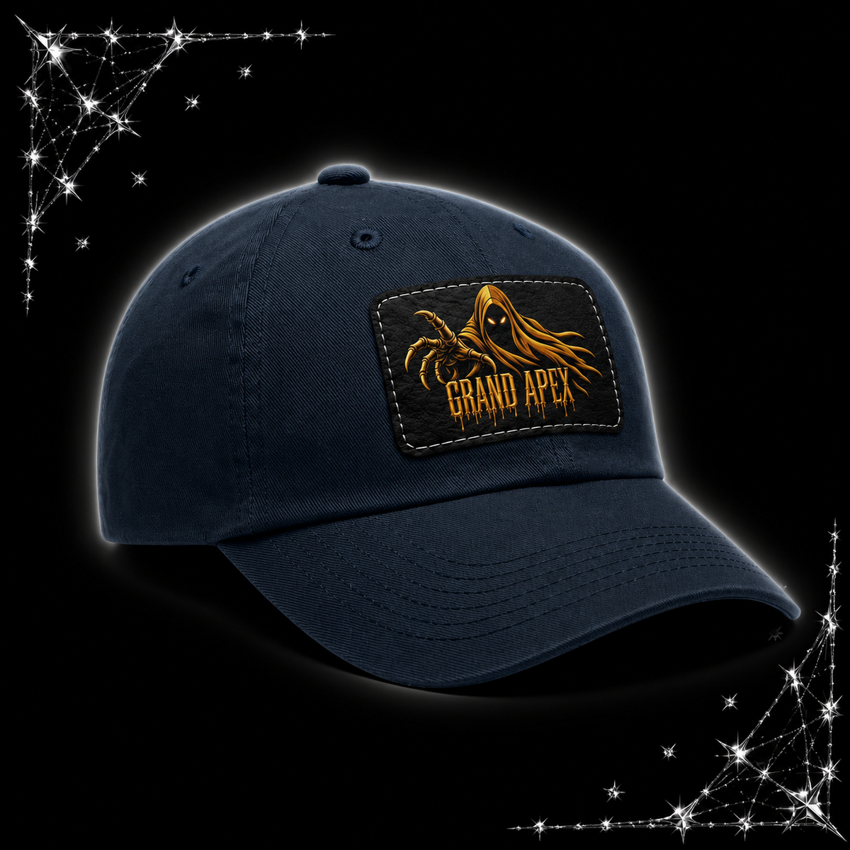 A blue/navy baseball cap with a rectangular front patch featuring a gold phantom graphic and the text 'GRAND APEX'. The cap is shown on a black background with chrome spiked webbing corner graphics.