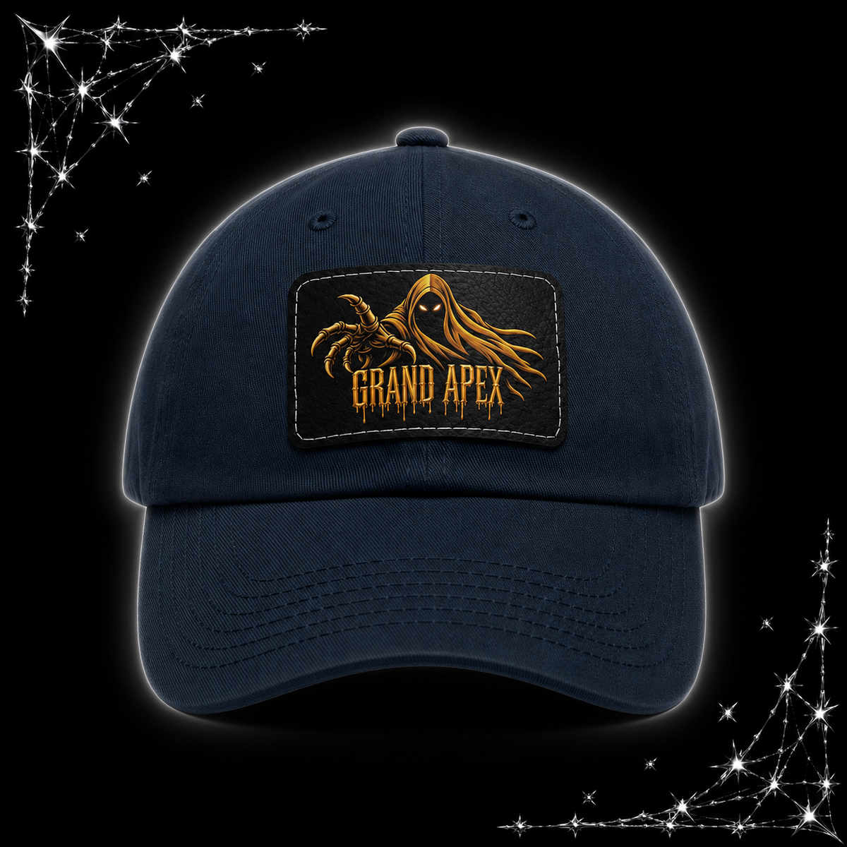 A blue/navy baseball cap with a rectangular front patch featuring a gold phantom graphic and the text 'GRAND APEX'. The cap is shown on a black background with chrome spiked webbing corner graphics.