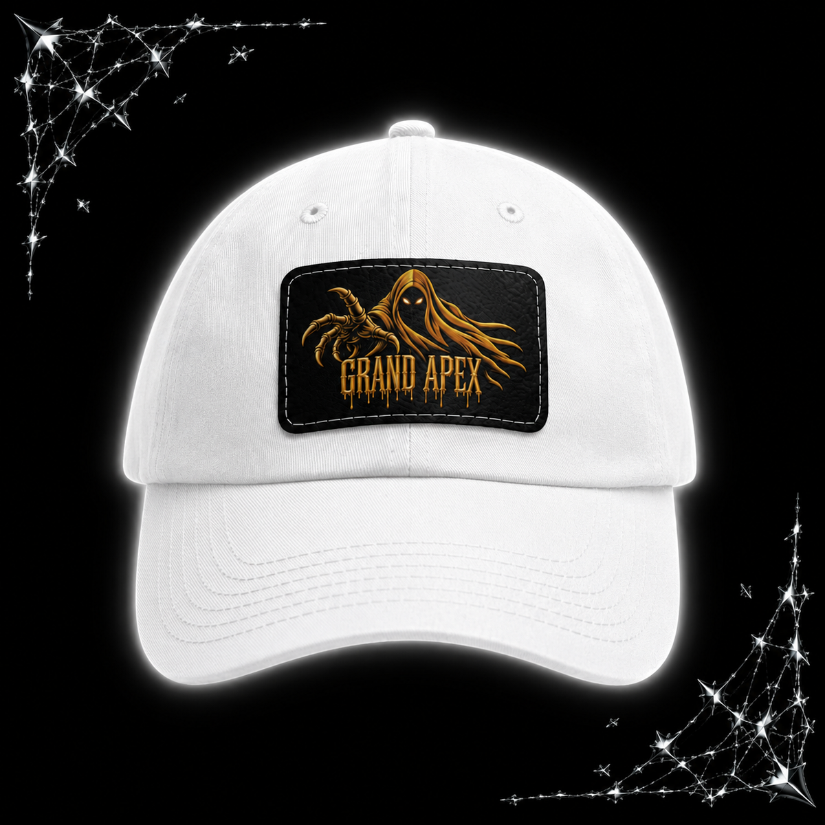A white baseball cap with a rectangular front patch featuring a gold phantom graphic and the text 'GRAND APEX'. The cap is shown on a black background with chrome spiked webbing corner graphics.